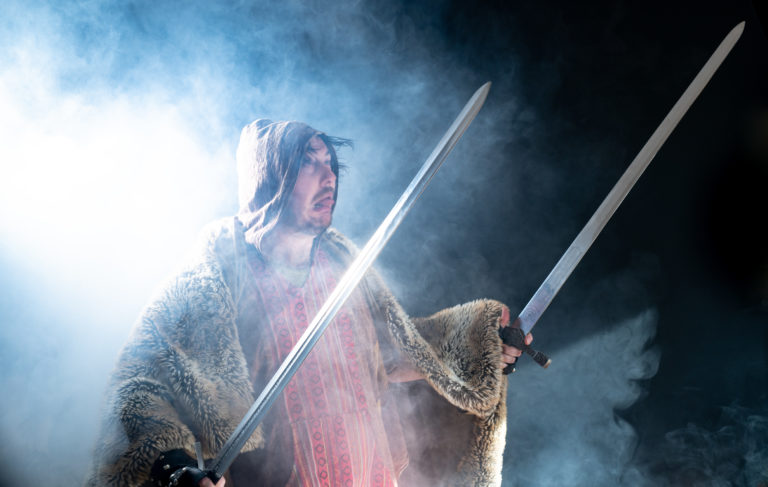 A guy holding two swords in lit up smoke and looking weird